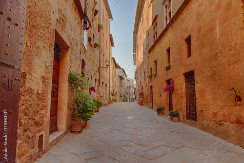 Beautiful narrow street with sunlight and flowers in the small magical and old village of Pienza  Val D Orcia Tuscany  Italy.