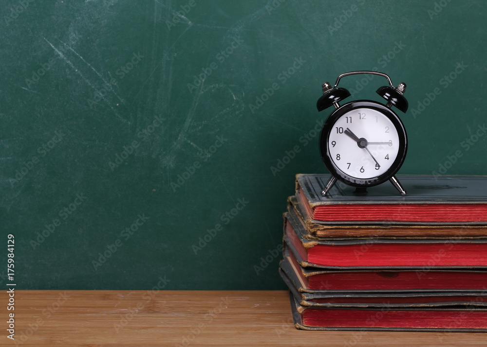 Small clock on books on desk, chalkboard background Small clock on books on desk, chalkboard background