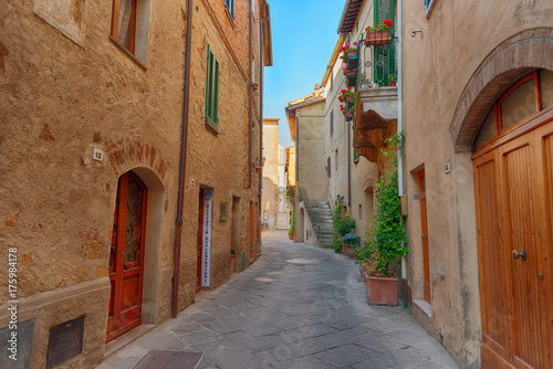 Fototapeta Naklejka Na Ścianę i Meble -  Beautiful narrow street with sunlight and flowers in the small magical and old village of Pienza, Val D'Orcia Tuscany, Italy.