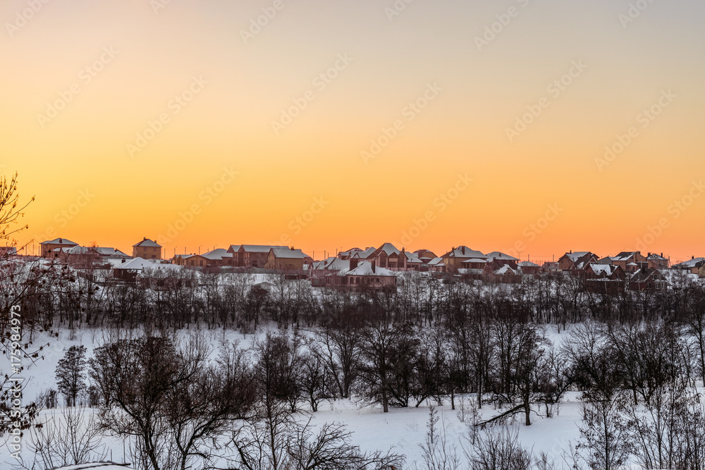 Evening winter sunset over suburban houses on horizont. Winter landscape with snowy village. Belgorod Region, Russia.