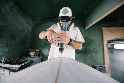 Shaper drilling hole into surfboard for leash plug installation photo