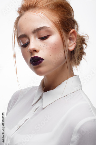 Young girl with a haircut in a white shirt. Beautiful model with nude make-up and bright lips. Office Style. Red-haired girl with freckles. Beauty of the face. Photo taken in the studio.