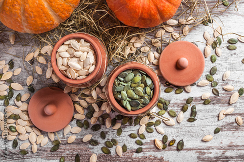 Colorful pumpkins and seeds in two ceramic jars on white rustic table with straw in studio