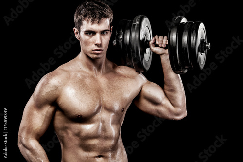 Athletic shirtless young sports man - fitness model holds the dumbbell in gym. Copy space fore your text.