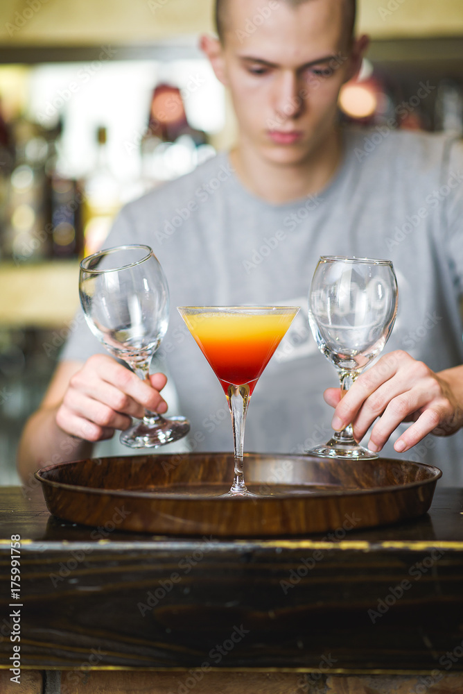 Young bartender making a colorful cocktail, pouring alcohol in a cocktail glass