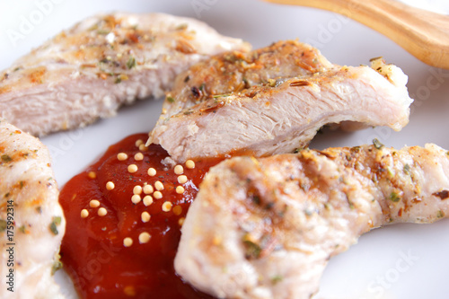 Steaks with grill on a white plate with a wooden fork, tomato sauce, spices and grains of mustard on a dark blue background in retro style