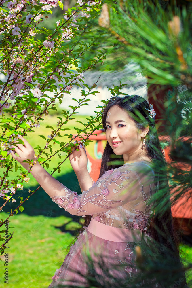 Lovely beautiful girl in pink dress standing near blooming cherry in the park Lovely beautiful girl in pink dress standing near blooming cherry in the park
