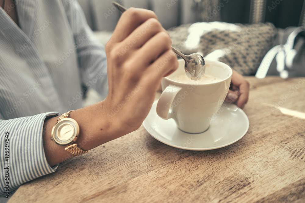 A girl is sitting in a cafe. Drinking tea. Coffee. White cup with coffee. Stir sugar. Holds a cup of coffee in his hand. Pastel shades. Close-up A girl is sitting in a cafe. Drinking tea. Coffee. White cup with coffee. Stir sugar. Holds a cup of coffee in his hand. Pastel shades. Close-up