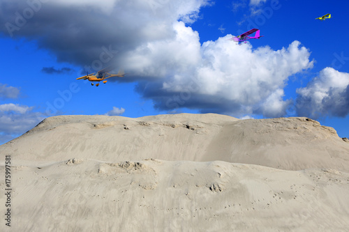 Trzy samolotu, awionetki w chmurach nad ogromną górą piachu.