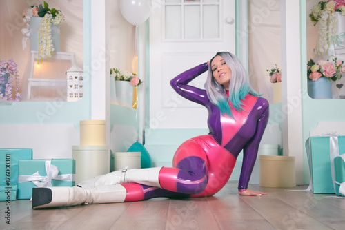 pretty anime girl wearing latex rubber doll catsuit and posing near cute white gift shop with air ballons and presents for christmas and new year photo