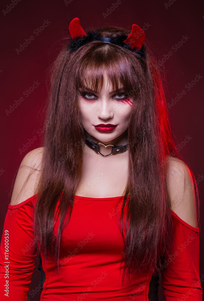 A beautiful, sexy woman in a devil costume, a demon with horns in a red dress. American, dress for a costume party Halloween. Choker on the neck. Bright makeup Photos
