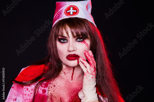 A beautiful, sexy woman, a vampire, a nurse all in blood, with a flow of blood on the face. Kill the killer, maniac. American, dress for a costume party Halloween. photo