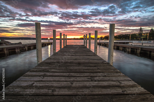 Wooden Dock On Sunrise Lake. Summer sunrise over the waters of Grand Traverse Bay in Traverse City, Michigan. Shot with long wooden dock in foreground sunrise over water at horizon. photo