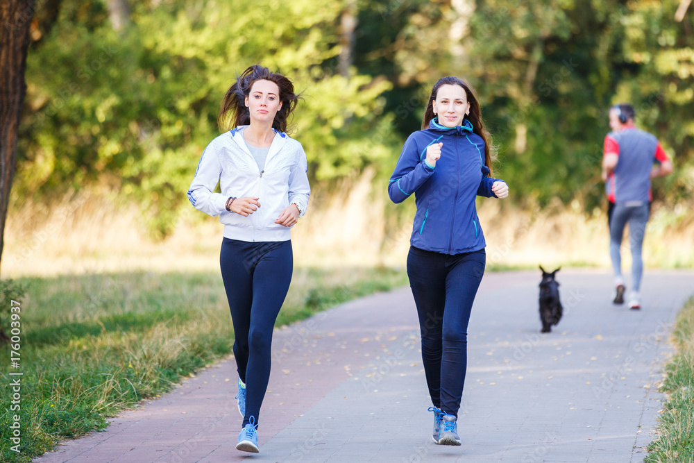 Two young smiling woman jogging in park in the morning Two young smiling woman jogging in park in the morning