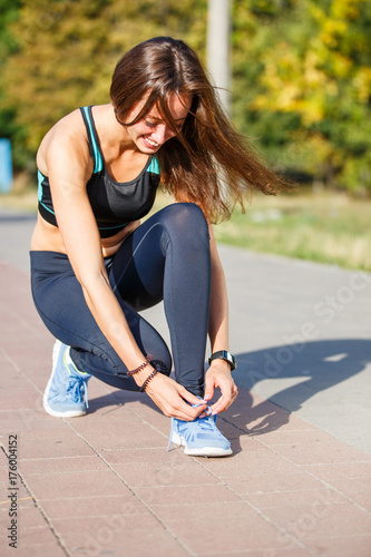 Young woman runner lacing up shoelaces on the trail jogging in park