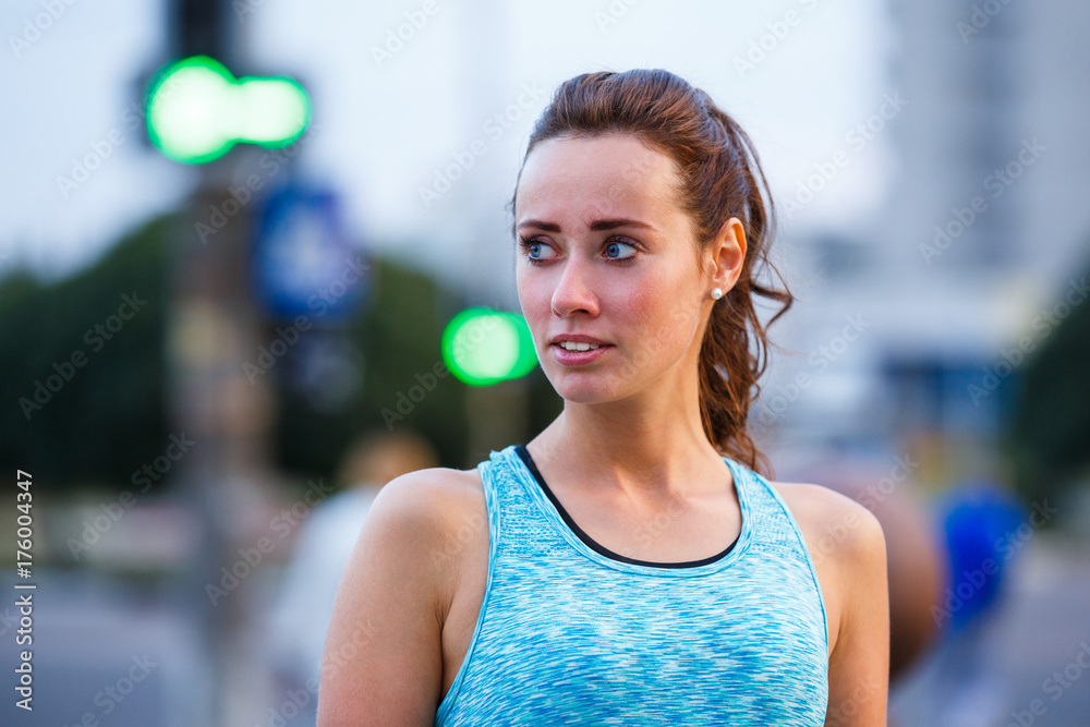 Portrait of young sporty woman resting after jogging in the evening city. Portrait of athletic girl in blue top at sunset