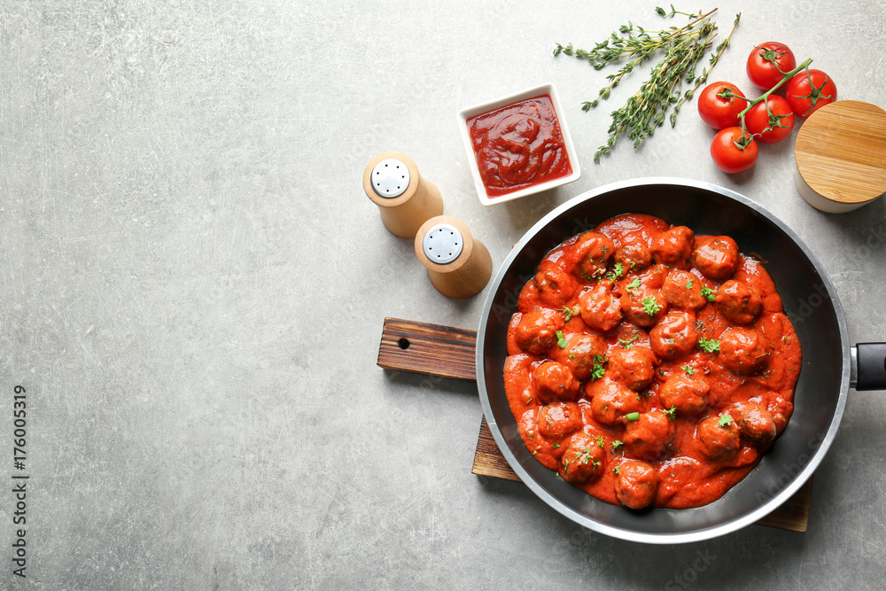Frying pan with delicious meatballs in tomato sauce on table