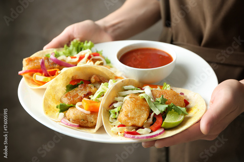 Woman holding plate with delicious fish tacos and tomato sauce, closeup