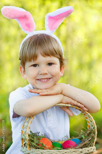 Easter bunny. Сhild with a basket of Easter colorful eggs. Kid, boy in a rabbit costume smiles.