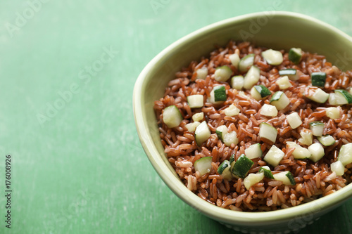 Bowl with tasty brown rice and zucchini on color wooden background