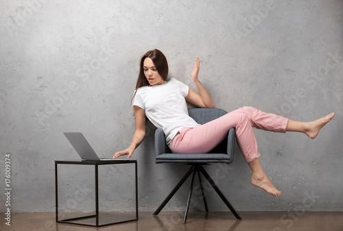 Young woman with laptop near grey wall