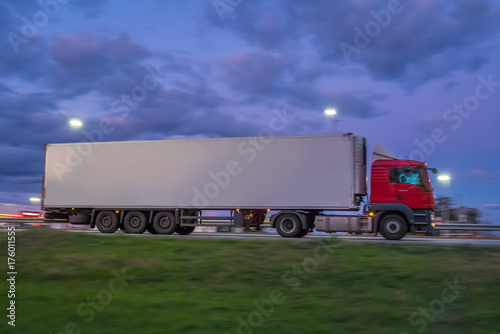 A large modern truck is driving along the highway in the night. 