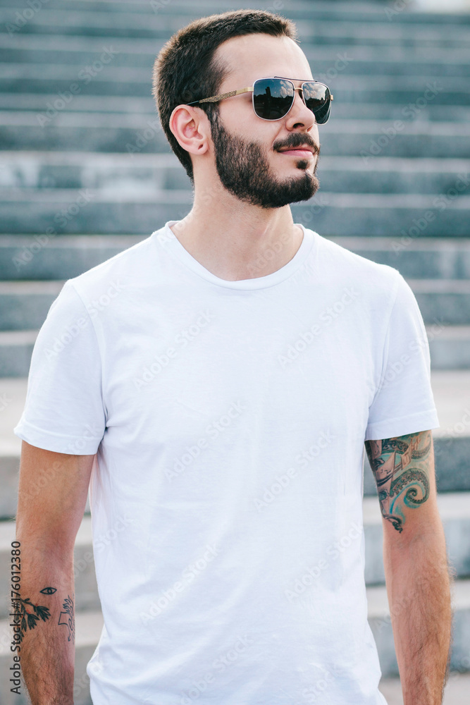 A stylish man with a beard in a white T-shirt and glasses. Street photo