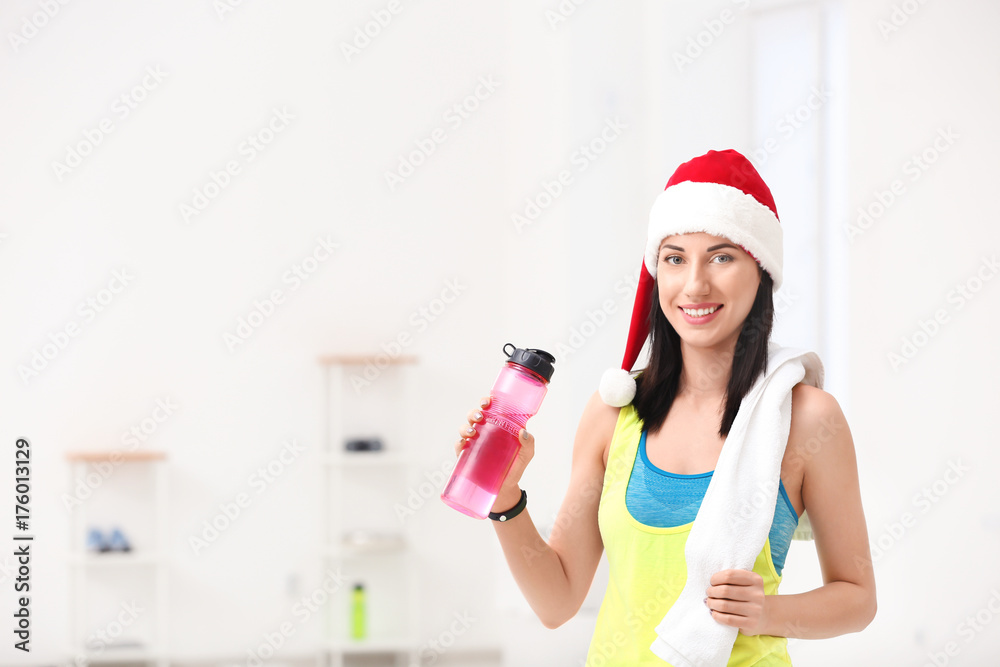 Φωτογραφία Beautiful young woman in Santa Claus hat with bottle of water at gym