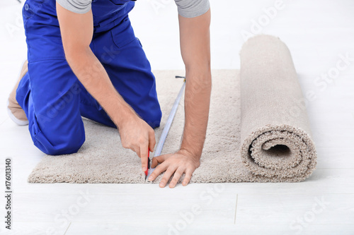 Male worker fitting carpet on floor indoors