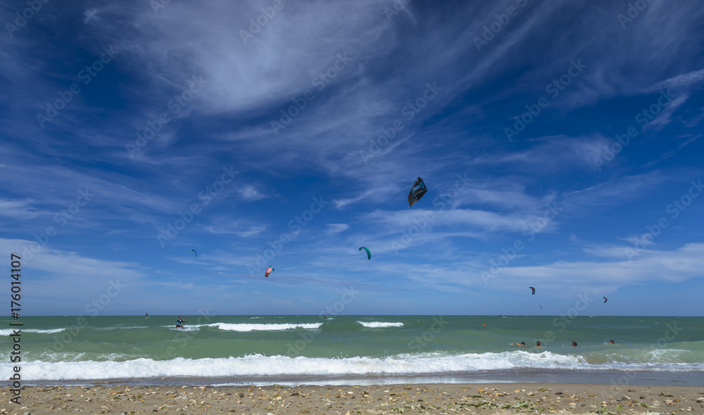 Panoramic view of kitesurfers sailing in a beach under beautiful clouds Panoramic view of kitesurfers sailing in a beach under beautiful clouds
