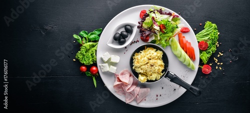 English breakfast. Eggs, olives, fresh vegetables, nuts, dried fruit and honey. Top view. Free space for text. On a wooden background.