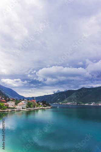 Travel picture natural landscape with blue sea of the boka bay and coast line with colors houses with red roofs, beautiful clouds and lobely boat. Vertical.