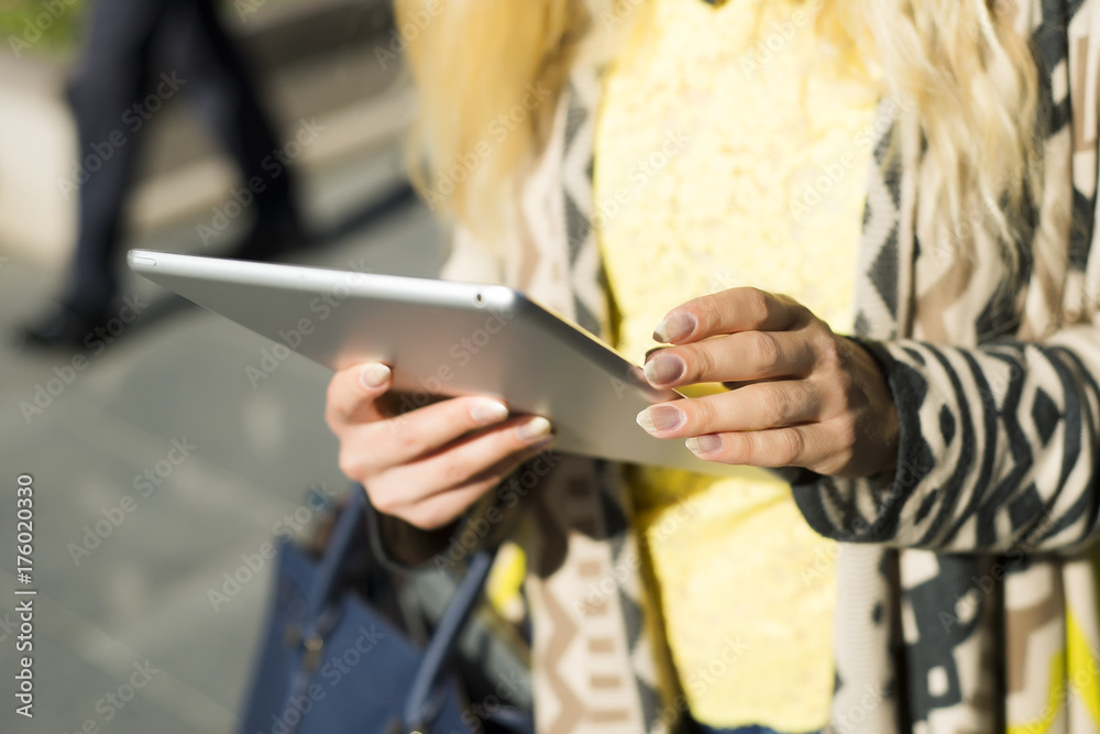 Young blond business woman using tablet computer walking in city street. Stylish fashion model in sunglasses