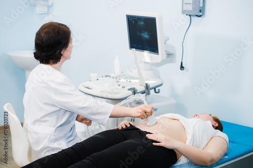 Pregnant woman looking at ultrasound shots of her growing baby showed by her doctor during medical examination