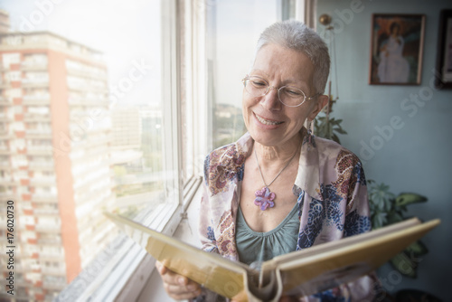 Bilde på lerret Senior elderly lady looking at some old photos in a photo album, remembering her