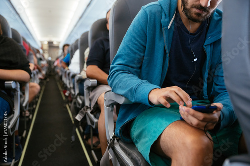 Young man using his phone with headphones in an airplane during a flight photo