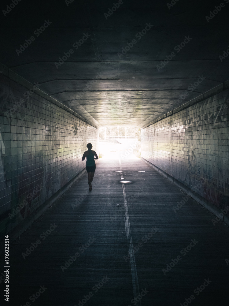 Woman running through tunnel towards bright light