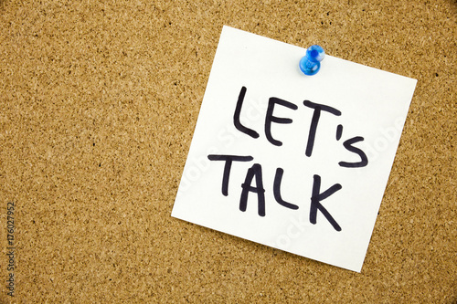 A yellow sticky note writing, caption, inscription Phrase LET'S TALK in black ext on a sticky note pinned to a cork notice board