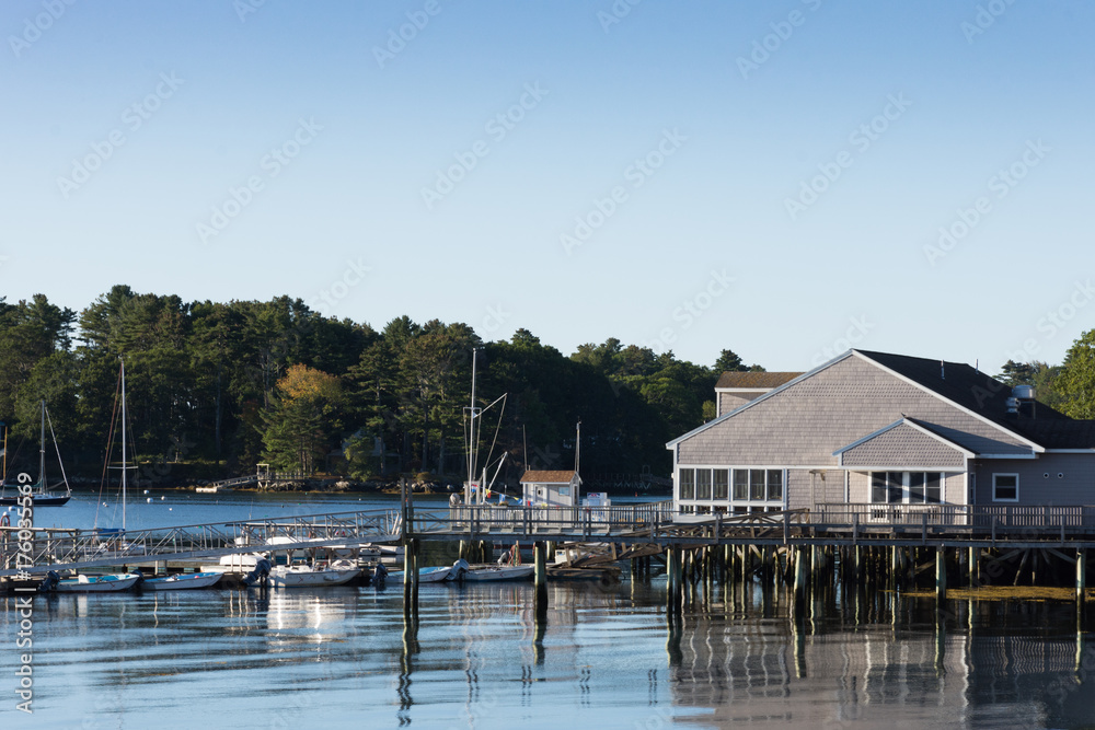 Boothbay Harbor Marina with sailboats and motorboats docked. A cloudless blue sky is above and provides copy space.
