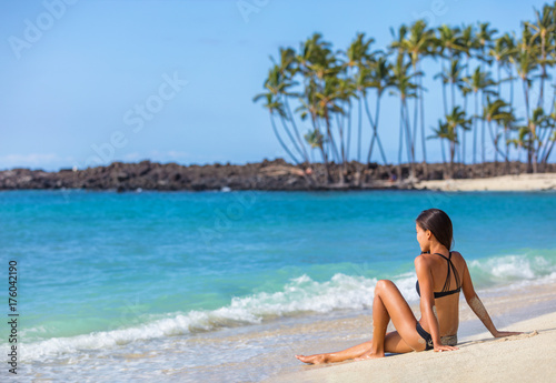 Bikini girl lying on sand sun tanning in Hawaii. Travel vacation woman relaxing on tropical nature relaxing landscape. Young person enjoying ocean view.
