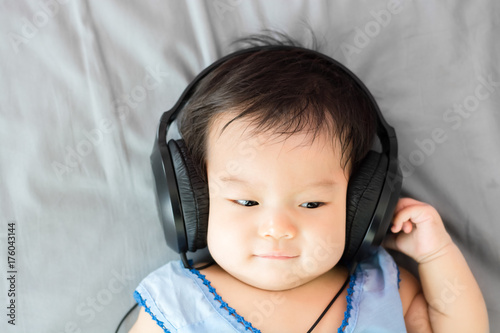 Portrait of adorable baby lying on the bed with headphone, indoors