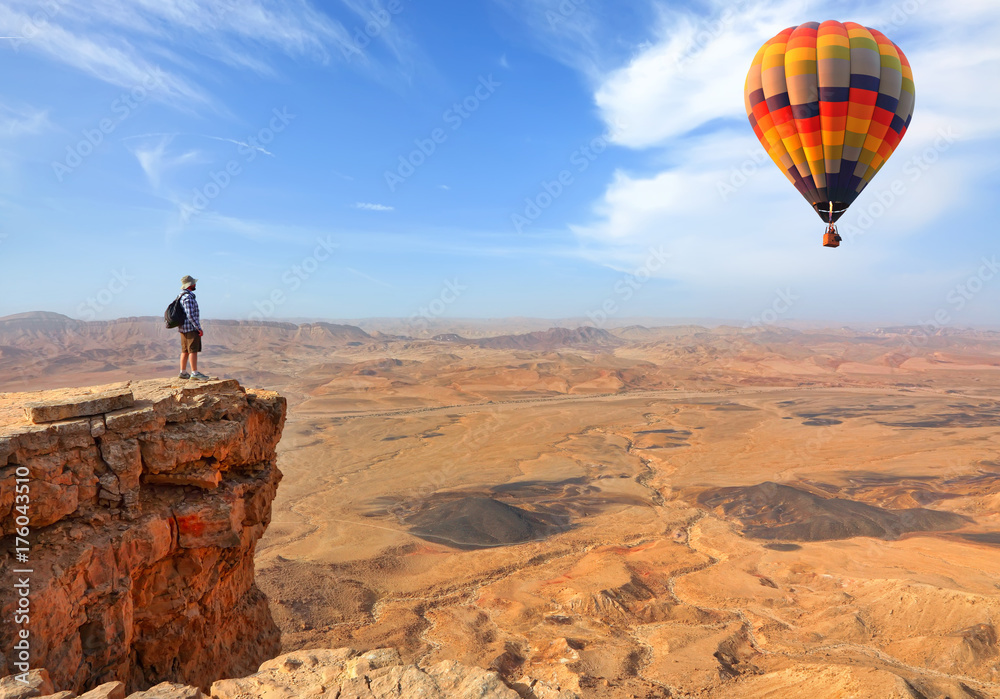 Fototapeta premium Beautiful landscape of stony desert and rocks and colorful hot air balloon flight in the blue sky. Traveler is on the mountain top viewpoint
