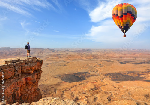 Beautiful landscape of stony desert and rocks and colorful hot air balloon flight in the blue sky. Traveler is on the mountain top viewpoint