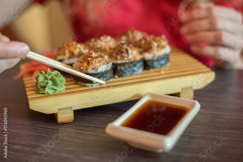 The girl eat Japanese food keeps sushi rolls with wooden chopsticks and moka them in soy sauce