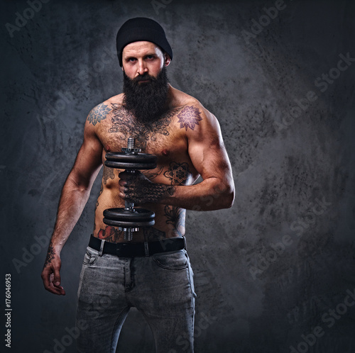 Shirtless muscular, bearded male holds dumbbell.