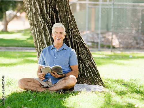 Senior man sittingin park while reading book photo