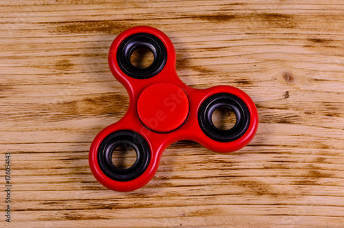 Red fidget spinner on wooden desk. Top view