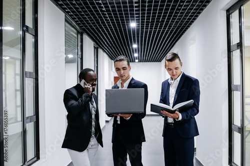 Three businessman standing in modern office with laptop and Notepad