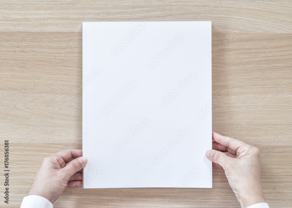 Fototapeta premium Blank A4 size book cover mockup template top view in businessman's hand with page front side on white surface flat lay on wood table