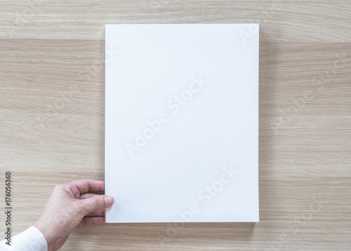 Blank A4 size book cover mockup template top view in businessman's hand with page front side on white surface flat lay on wood table © Chinnapong